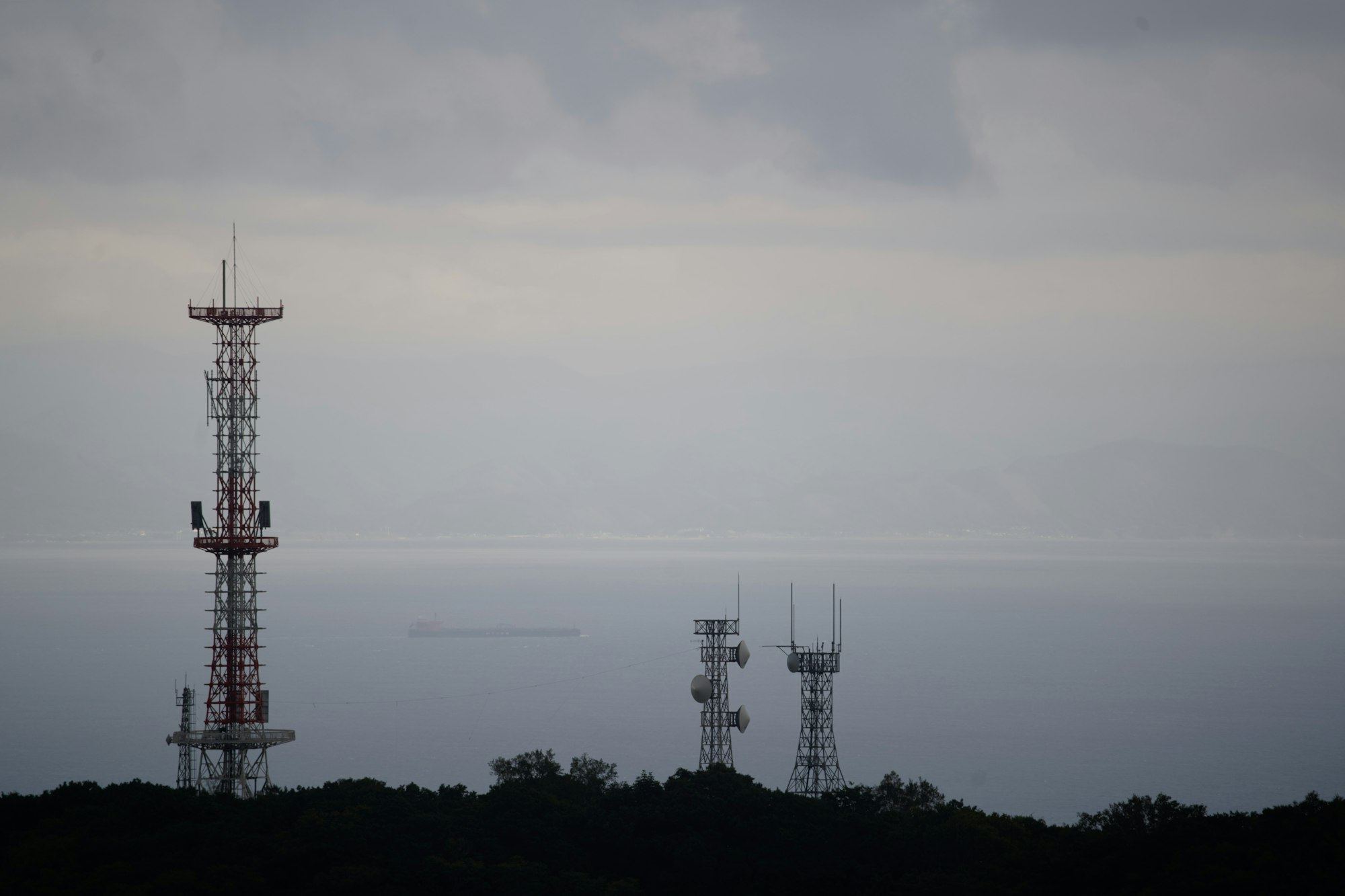 Communication towers on a forested ridge above the sea